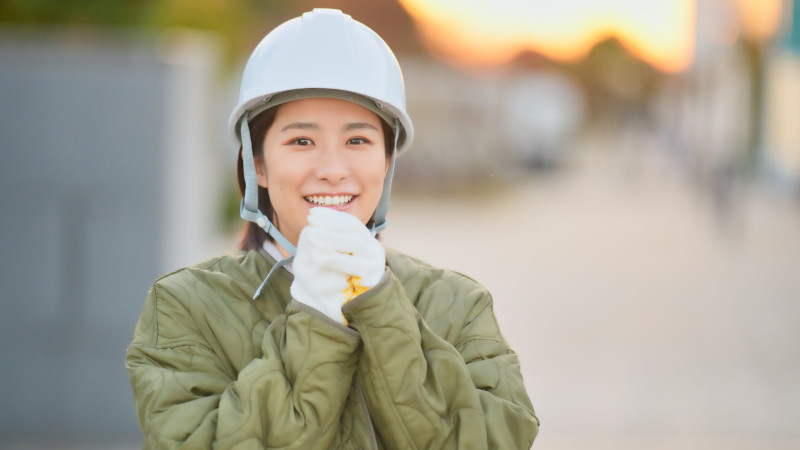 作業現場で防寒着のアウターと作業用手袋と作業用安全ヘルメットを身に着けた女性のイメージ画像